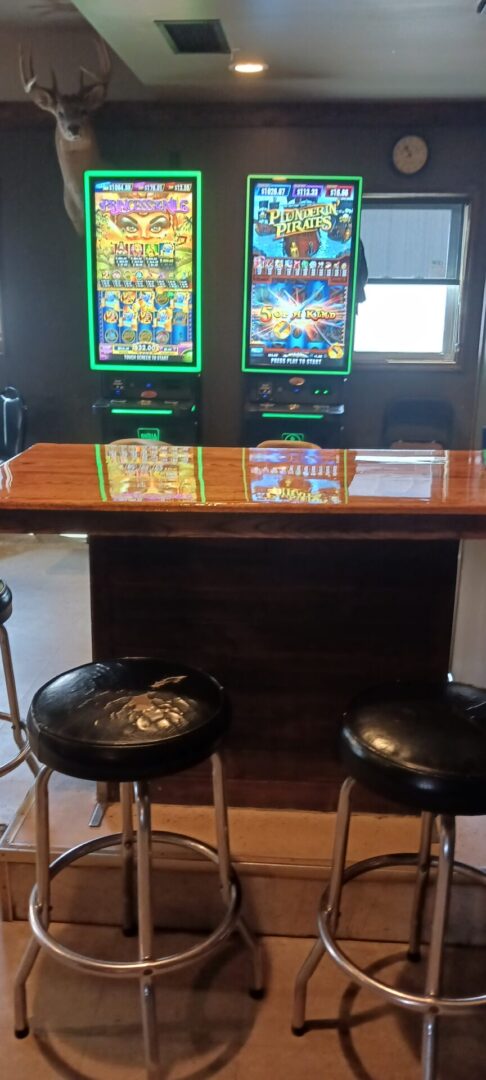 A table with two chairs and two tvs in the background.