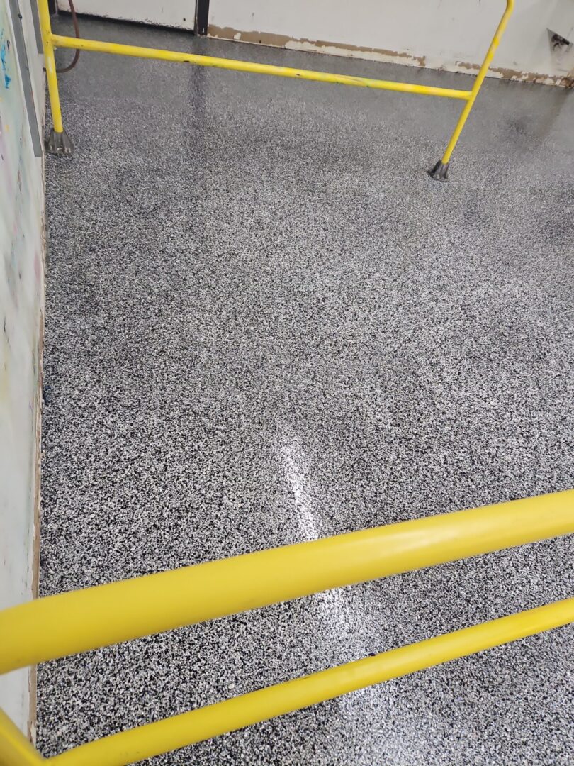 A yellow railing and some steps with a floor covered in gravel