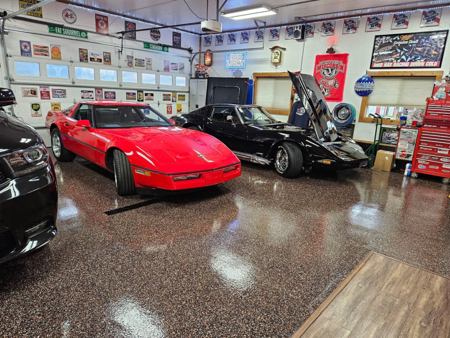 A red corvette parked in front of a black car.